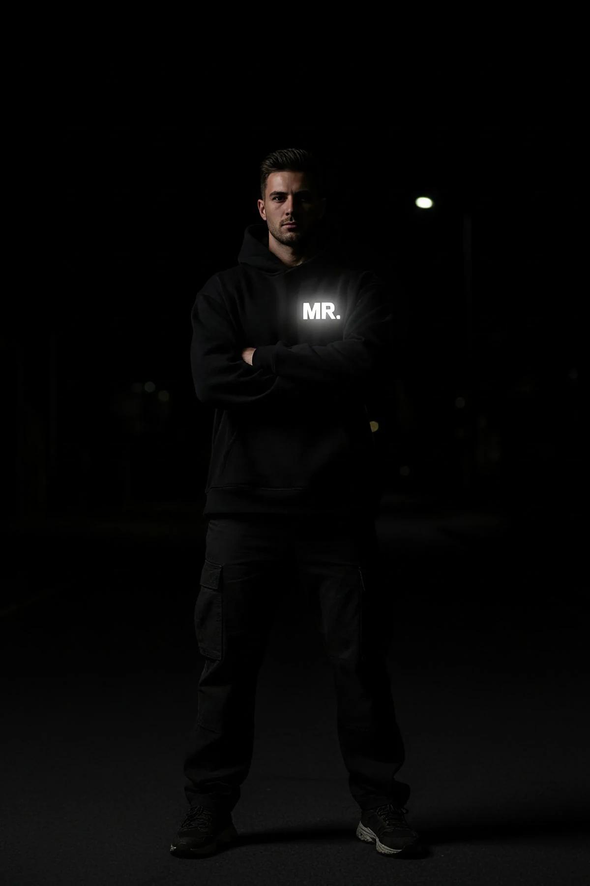 Reflective black hoodie with glow-in-the-dark MR. chest print worn in dark setting