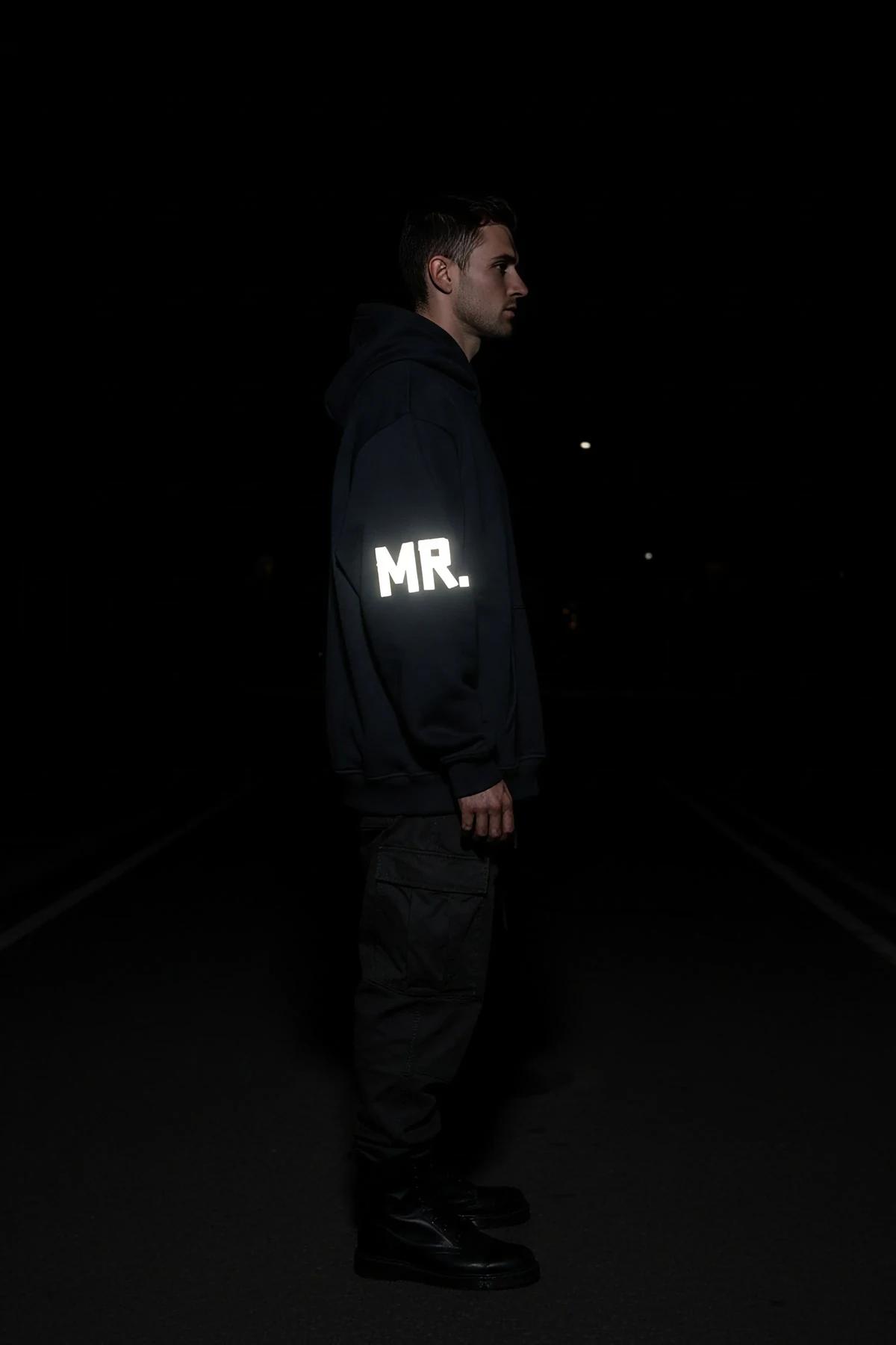 Reflective black hoodie with glow-in-the-dark MR. sleeve print shown in nighttime street setting
