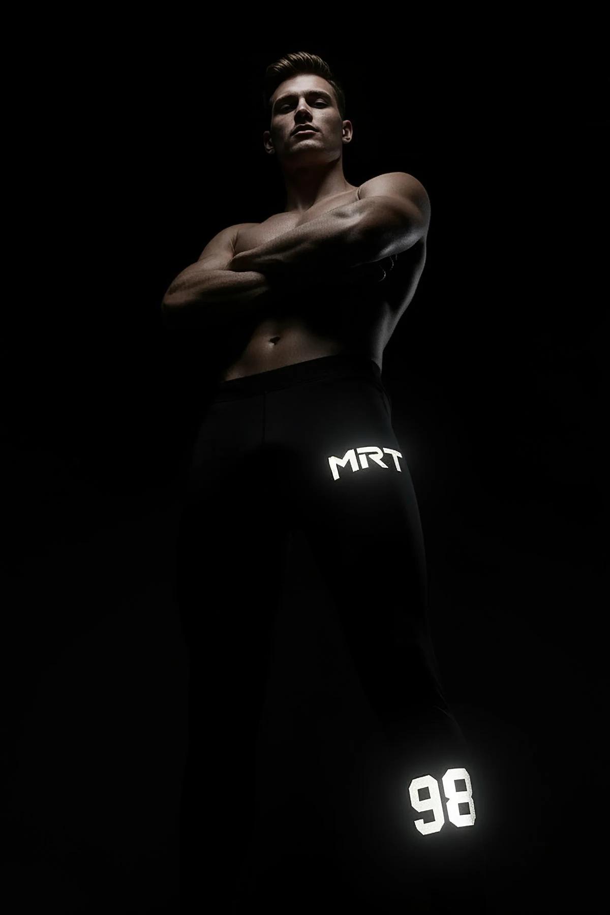 black reflective sport joggers with white MRT logo on thigh and number 98 near ankle hem glowing under light