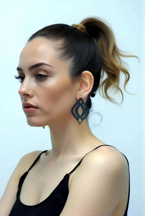 Black matte vegan leather drop earrings with geometric cut-out motif worn by a model with a high ponytail