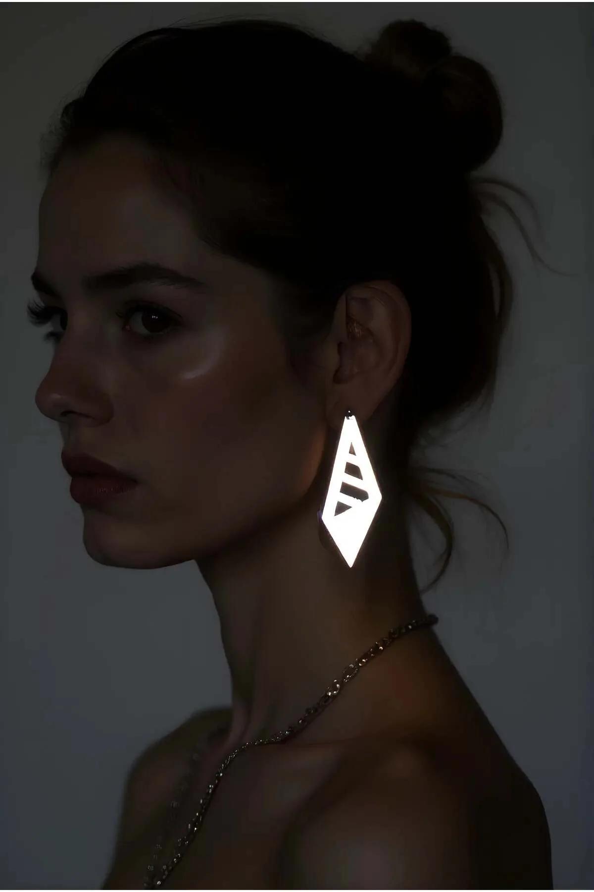 Reflective silver laser-cut prism drop earrings with geometric chevron cutout slots worn by model in low-light setting