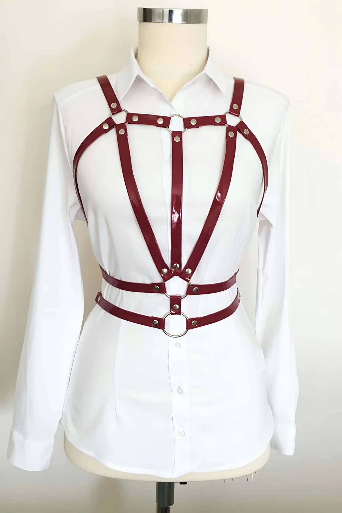 Burgundy glossy faux leather chest harness with silver rivets and dual O-rings layered over white shirt on mannequin