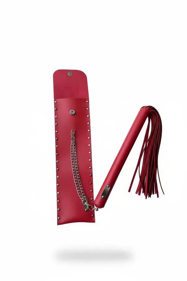 Red faux leather whip with cylindrical handle and tassel fringe beside open silver-studded red sheath with chain