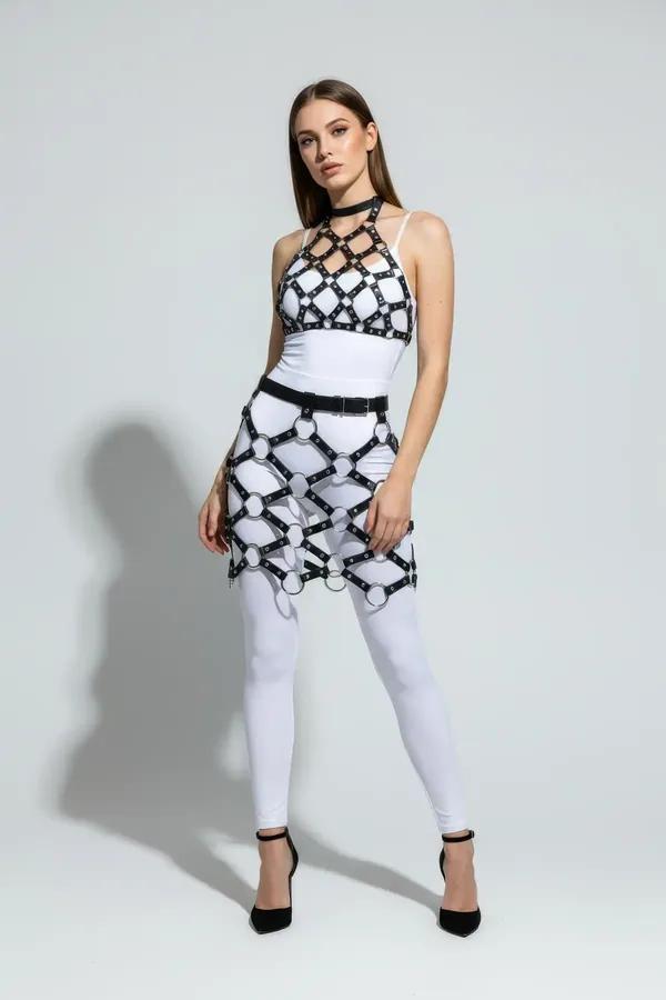 Black faux leather caged skirt harness with large silver O-rings worn over white bodysuit and leggings, full-length view