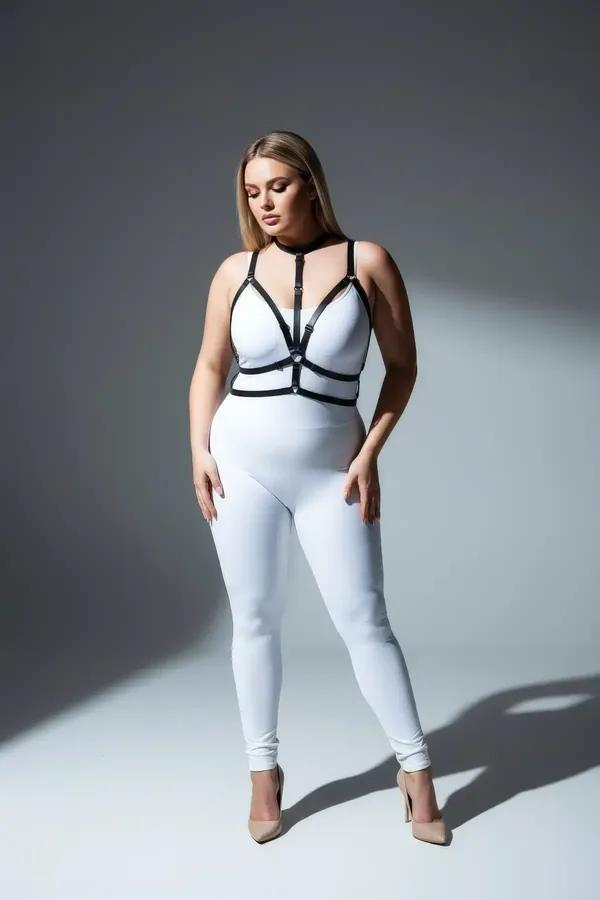 black faux leather strappy chest harness with collar neck strap and central silver O-ring worn over white bodysuit