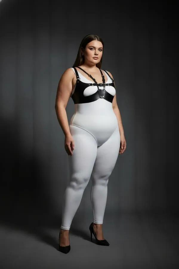 black faux leather harness bra with silver O-ring buckle and oval cut-out chest panel on plus-size model