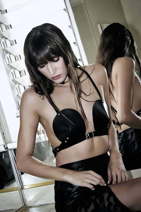Black faux leather underbust harness bra with structured molded cups and center silver buckle band on model