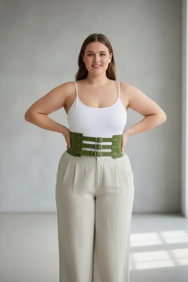 olive green faux leather wide waspie belt with three silver prong buckles worn over white bodysuit and cream trousers