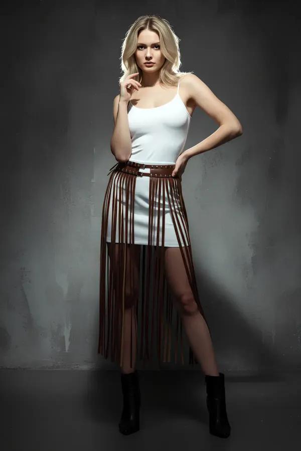 Brown faux leather fringed skirt harness with silver studded waistband worn at natural waist over white mini dress