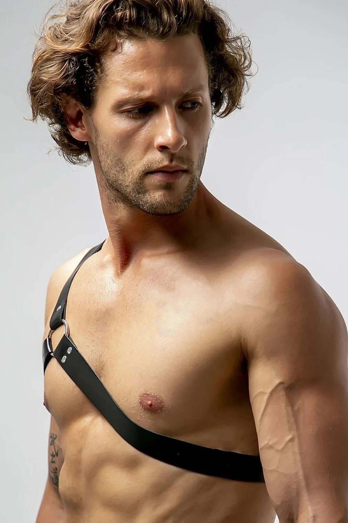 black asymmetrical faux leather chest harness worn over bare chest diagonal strap detail