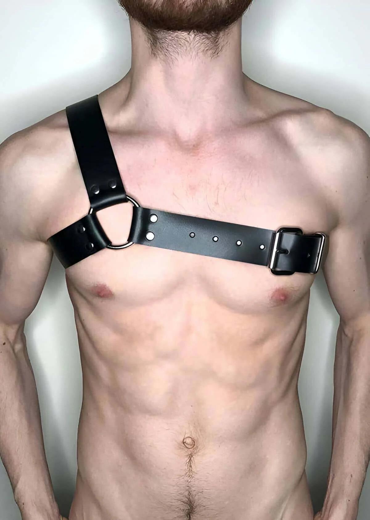 Black faux leather asymmetrical chest harness with wide 4 cm strap, silver O-ring center, and matte-black rectangular buckle 