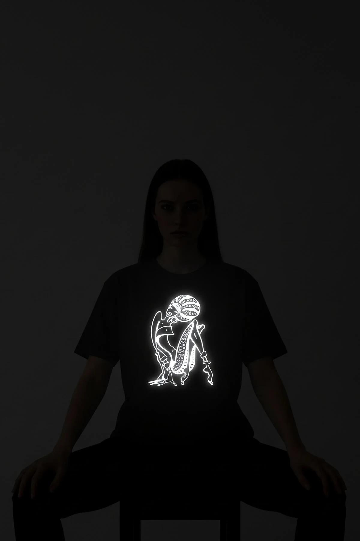 black reflective graphic t-shirt with bold custom text glowing bright white on chest in low-light studio shot