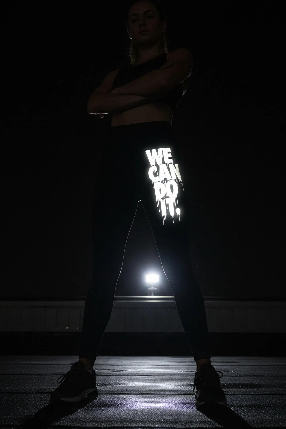 black high-waist leggings with white retroreflective We Can Do It graffiti-drip print on left thigh photographed at night