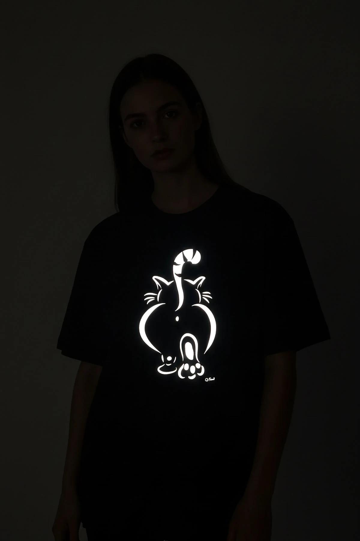 black oversized t-shirt with white reflective custom text print glowing against dark background