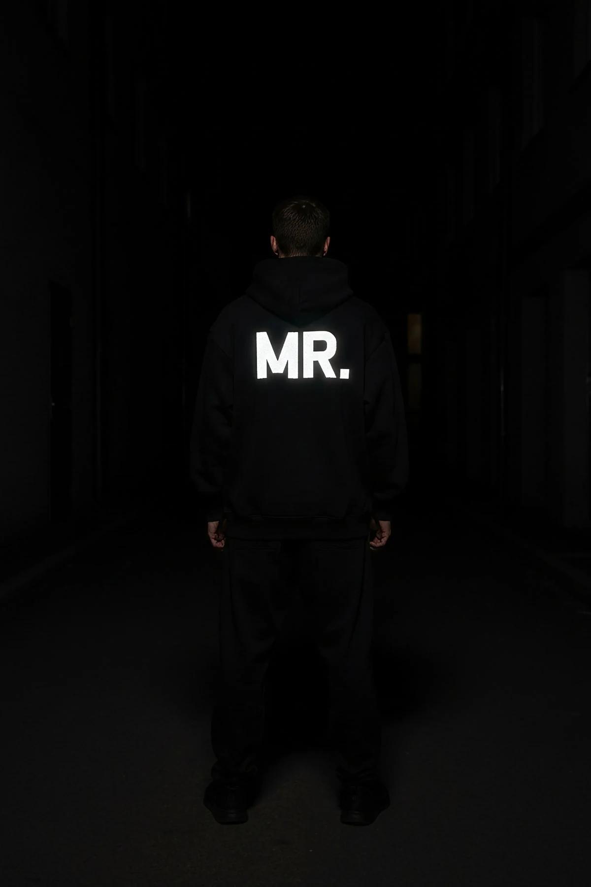 black oversized Mrs. hoodie with white reflective glow-in-the-dark MRS. block-letter sleeve print photographed at night