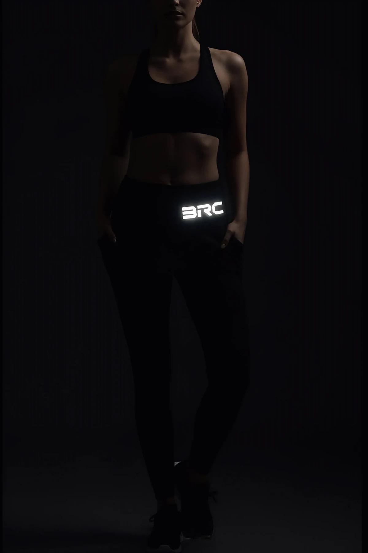 black high-waisted performance leggings with reflective logo print on outer thigh worn in dark gym setting