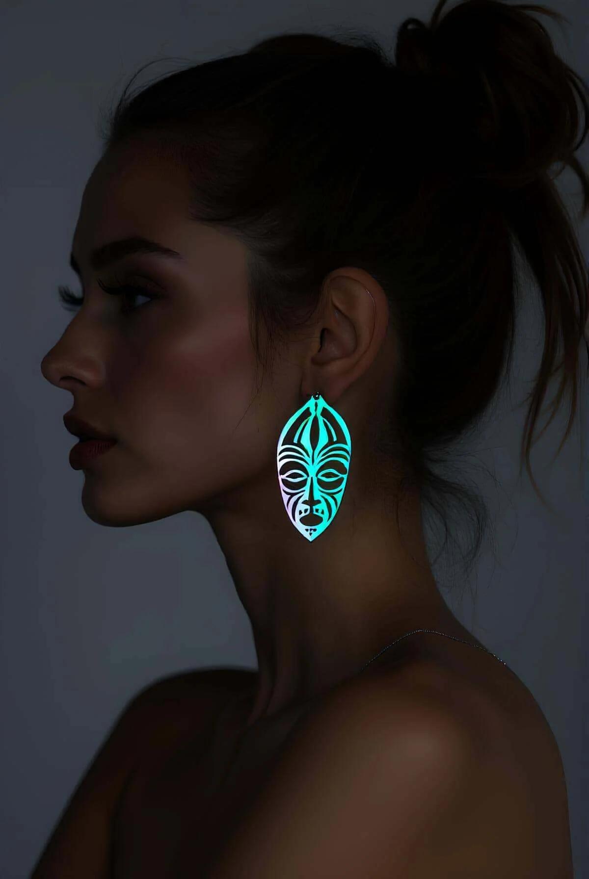 Reflektörlü lazer kesim etnik yüz küpe turkuaz ışık yansımalı oval tribal maske motifi karanlık arka plan