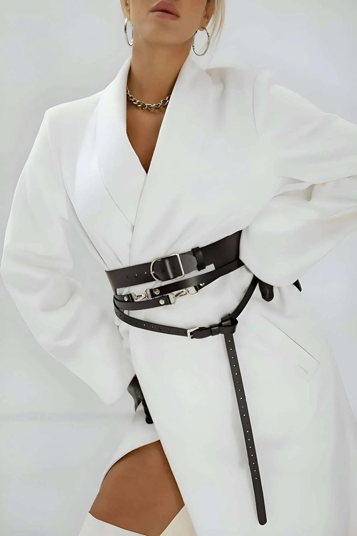 Black faux leather adjustable waist harness belt with silver buckles and trailing strap worn over white blazer
