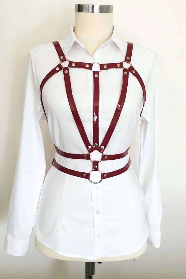 Burgundy glossy faux leather chest harness with silver rivets and dual O-rings layered over white shirt on mannequin