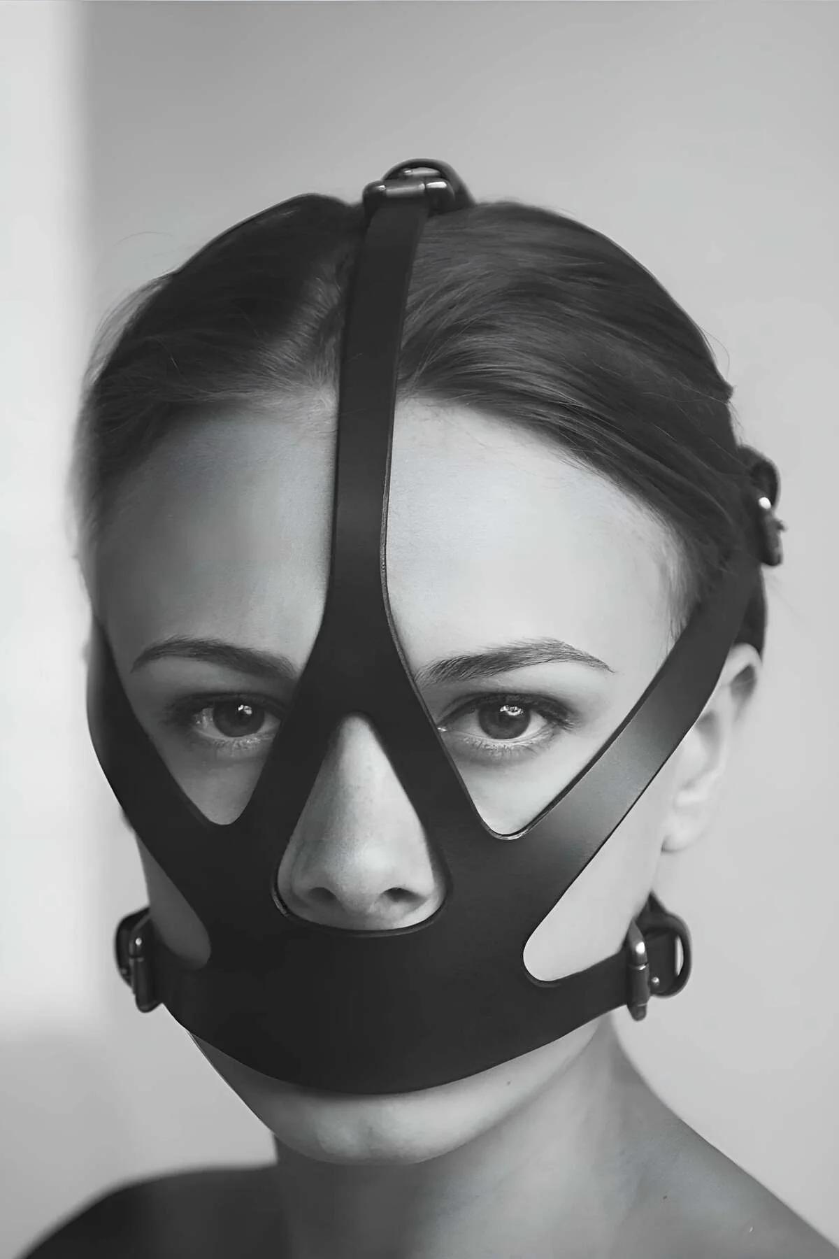Black faux leather face mask harness with geometric strap cutouts and silver O-ring closures worn front-facing