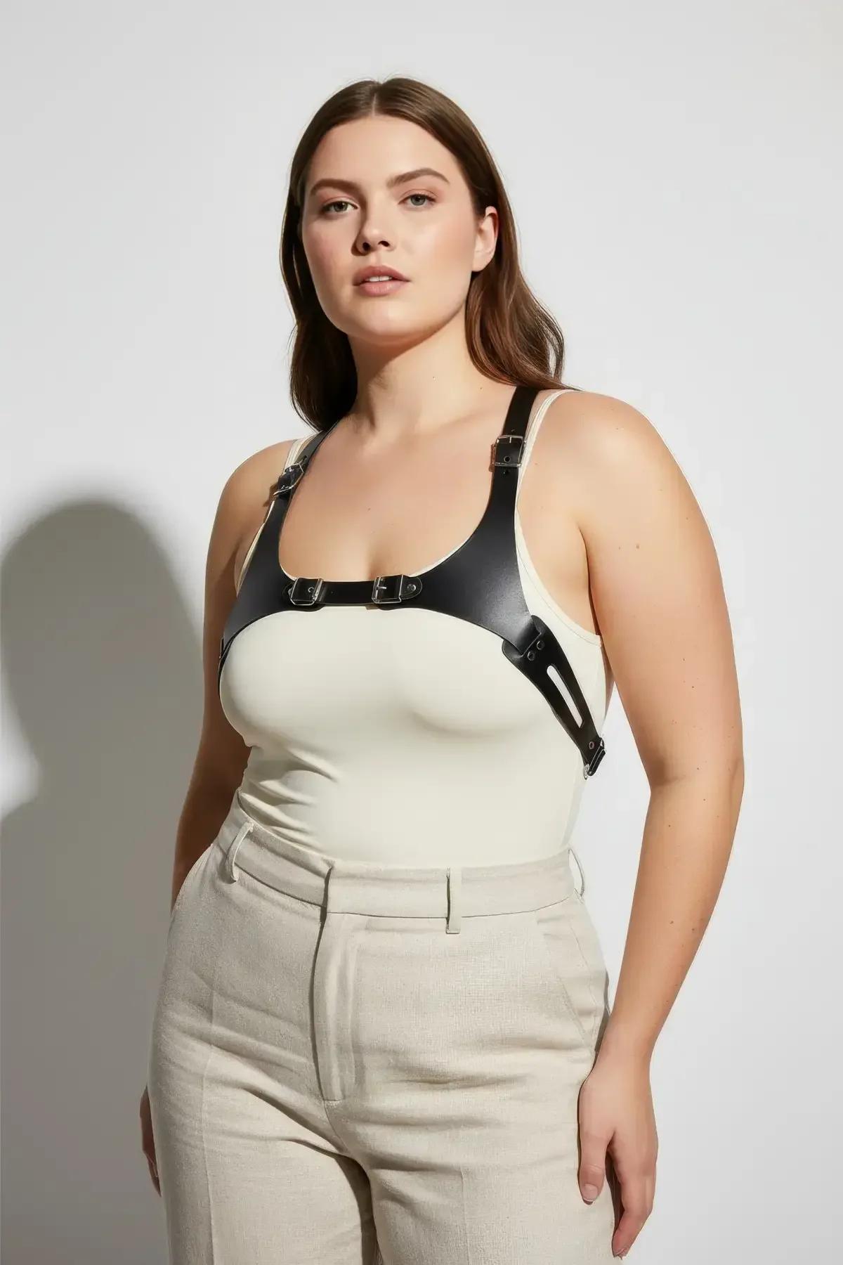 black faux leather chest harness with wide underbust band and dual silver rectangular buckles worn over cream bodysuit