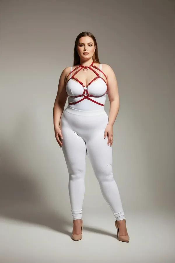 red faux leather cage harness bra with gold O-rings worn over white bodysuit plus size model