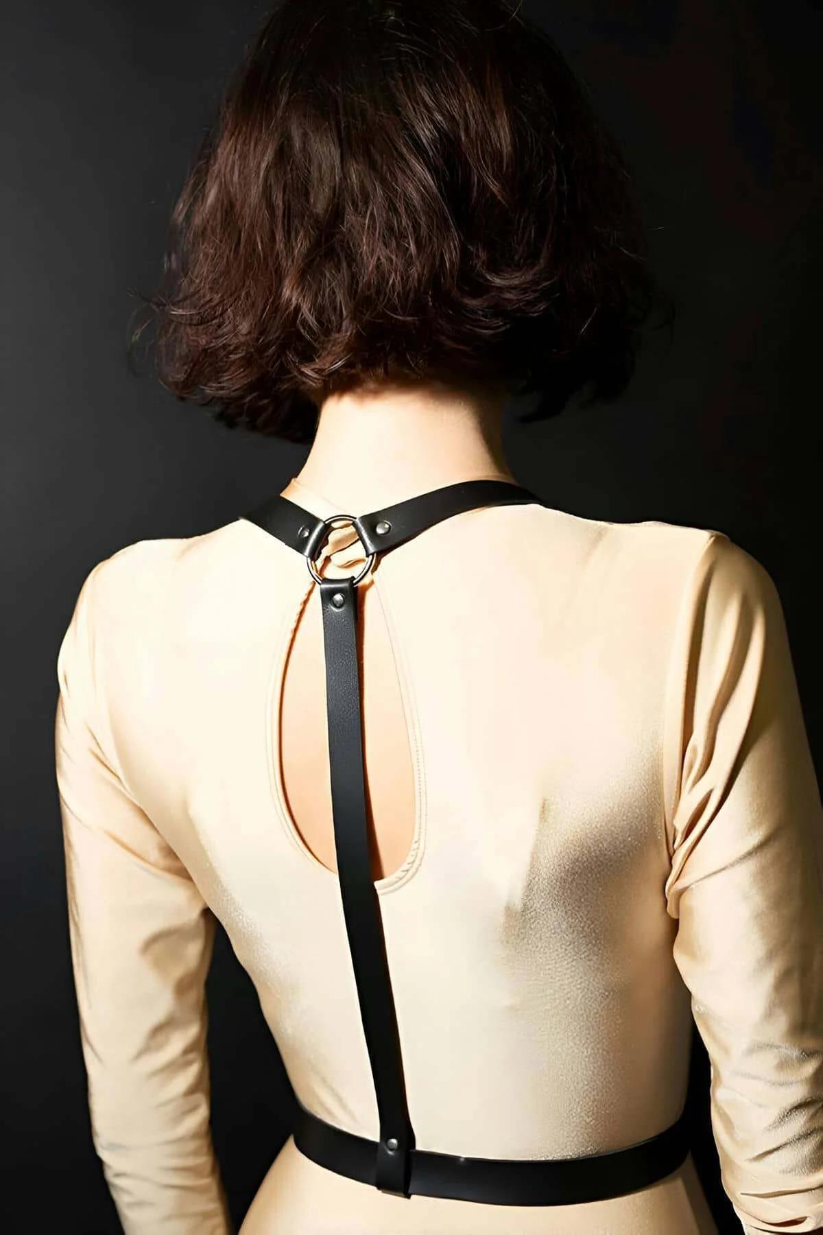Black faux leather O-ring body harness back view with gold-tone buckle hardware over cream top