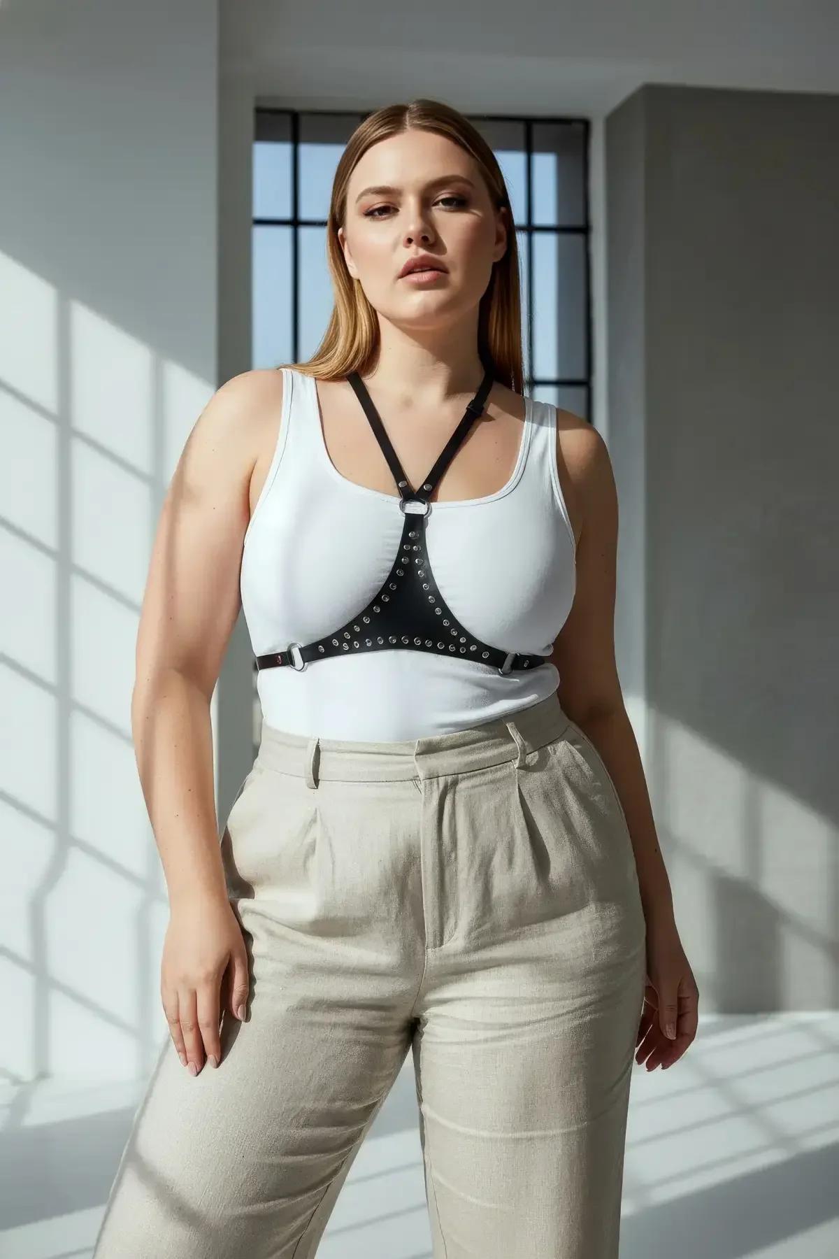 Black faux leather chest harness with silver metal studs and center O-ring, worn over white tank top