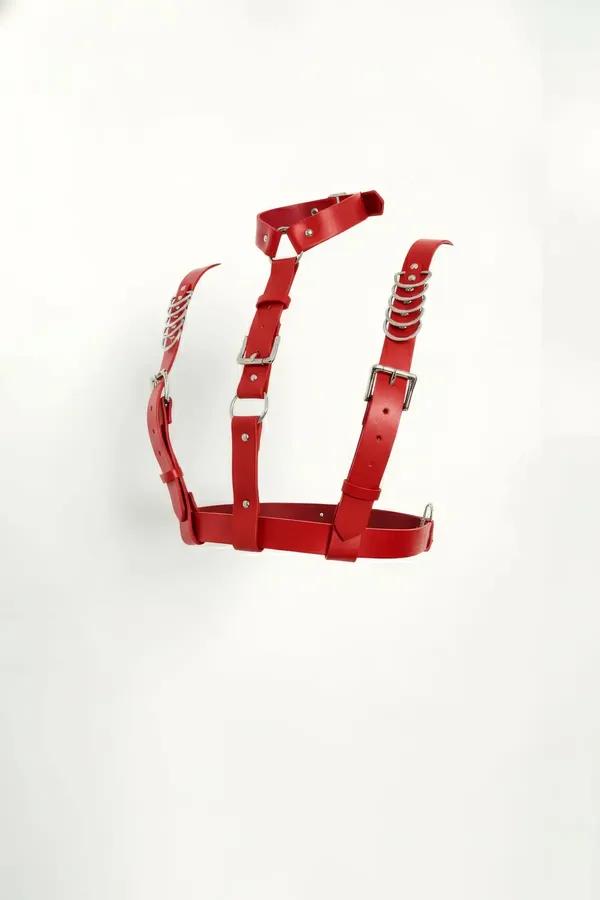Red faux leather chest harness with silver chain O-rings and pin-buckle closures, structured cage silhouette on white backgro