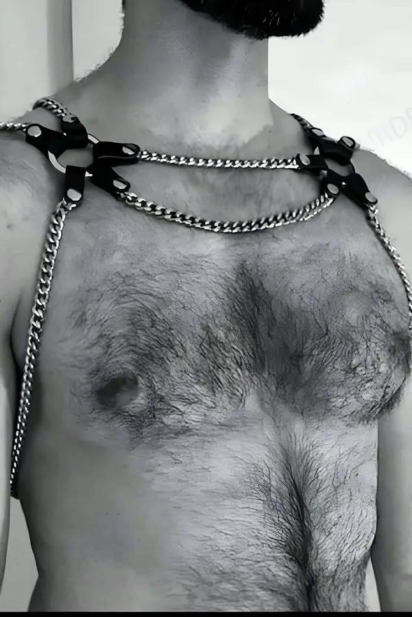 black faux leather shoulder harness with silver curb-link chains on male torso, adjustable strap tabs