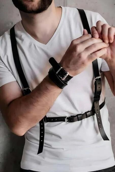 black faux leather chest harness with dual shoulder straps and silver buckles worn over white t-shirt with matching wrist cuf