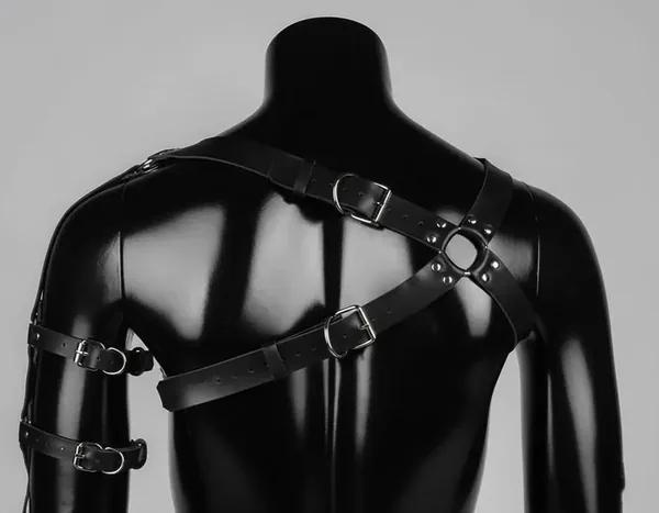 black vegan leather asymmetric chest harness with single shoulder strap, two silver O-rings, rivet studs, and separate upper