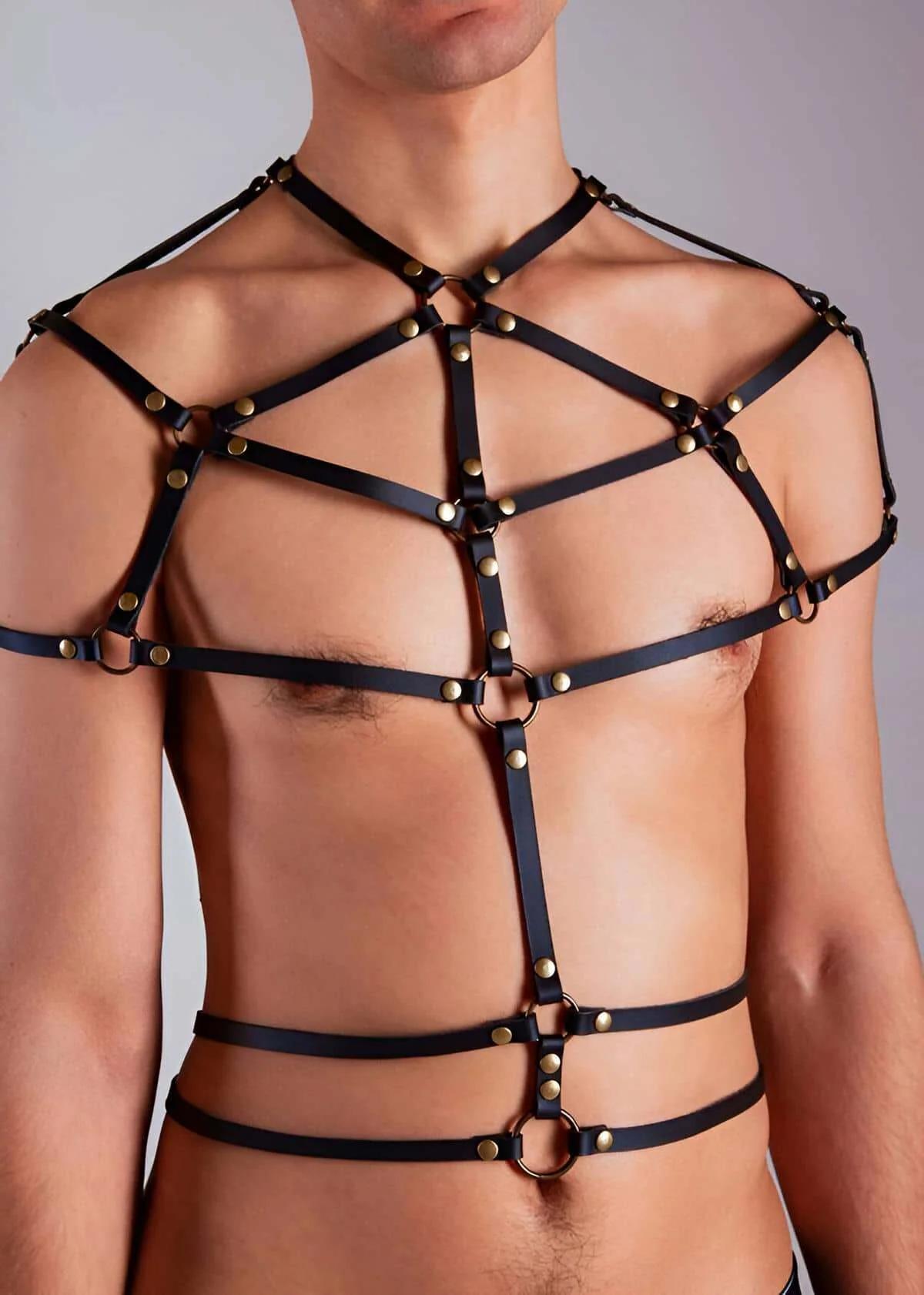 Black full body chest harness with antique brass O-rings and dome rivets worn on male torso showing geometric strap grid