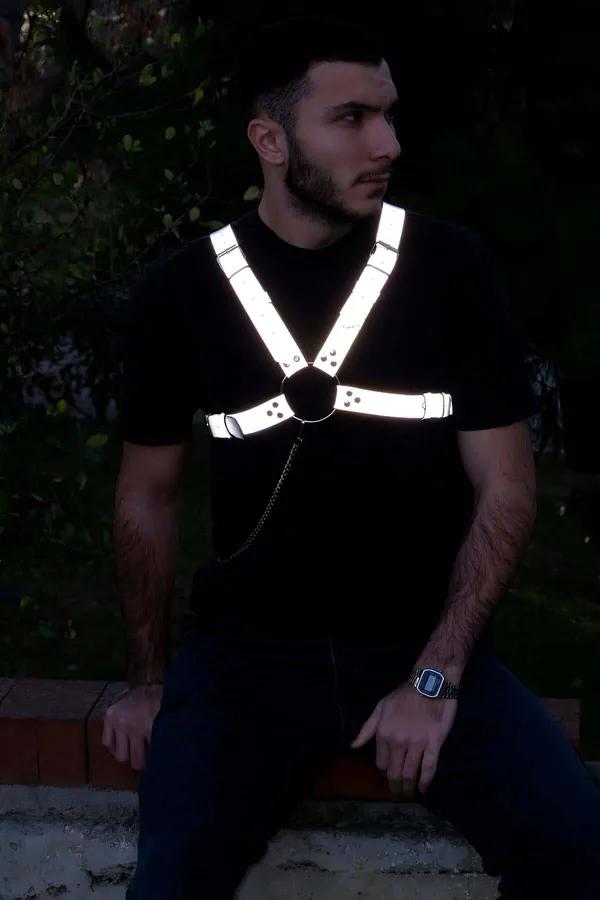 Reflektörlü gri erkek göğüs harness, ışık altında beyaz-gümüş parıltı, siyah O-ring ve metal zincir detayı