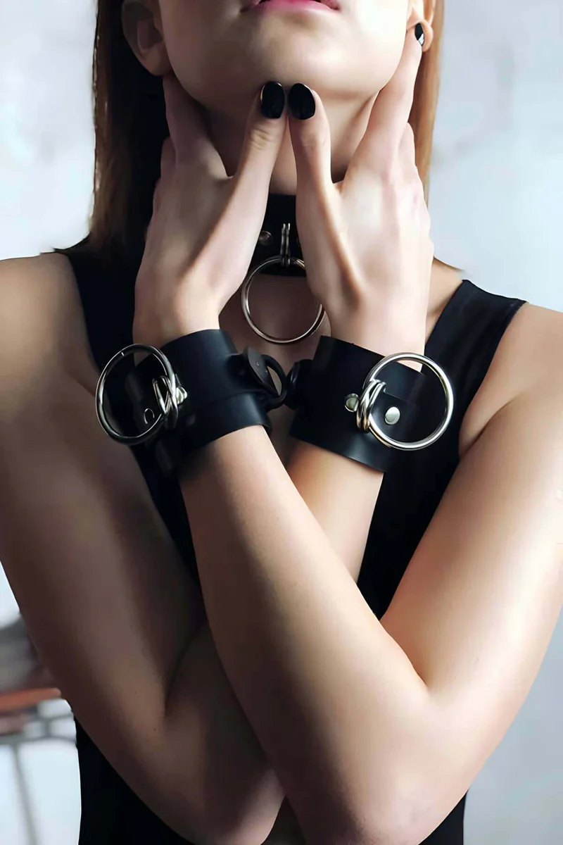 Black faux leather choker and cuffs set with silver hardware close-up.