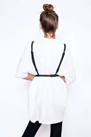 Black faux leather adjustable chest harness with central O-ring, worn over a white shirt.