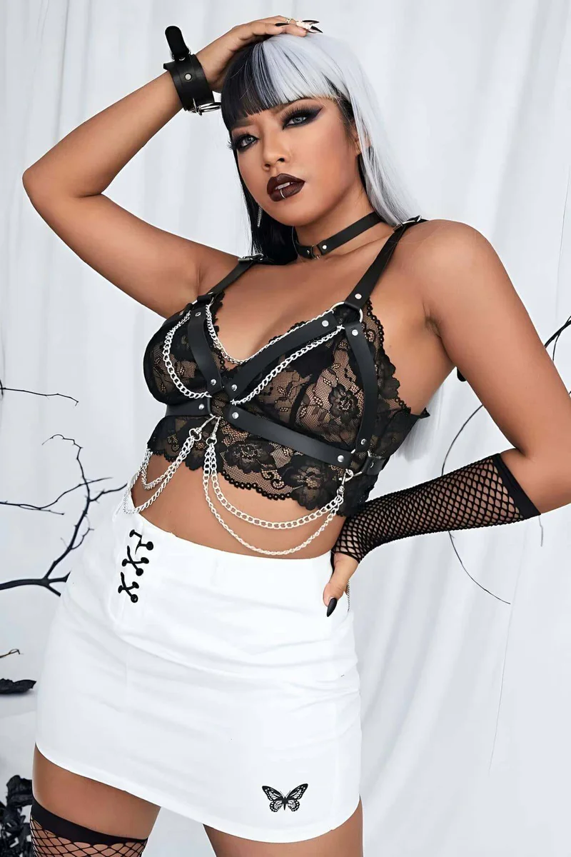 Fashion model wearing black faux leather chest harness over lace top with metal rings and chains