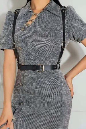Black faux leather adjustable body harness belt with silver buckle worn over a grey dress